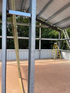 Exterior view of a commercial steel-frame warehouse building under construction, showing the open structural framing and concrete foundation.