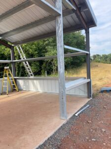 Exterior view of a commercial steel-frame warehouse building under construction, showing the open structural framing and concrete foundation.
