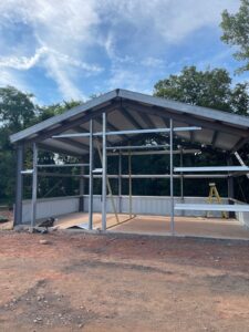 Exterior view of a commercial steel-frame warehouse building under construction, showing the open structural framing and concrete foundation.